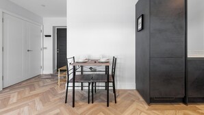 Eine moderne Küche mit einem dunklen Schrank, einem Essplatz mit weißen Tellern und Gläsern sowie einem Holzboden mit Zickzackmuster.