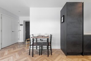 Eine moderne Küche mit einem dunklen Schrank, einem Essplatz mit weißen Tellern und Gläsern sowie einem Holzboden mit Zickzackmuster.