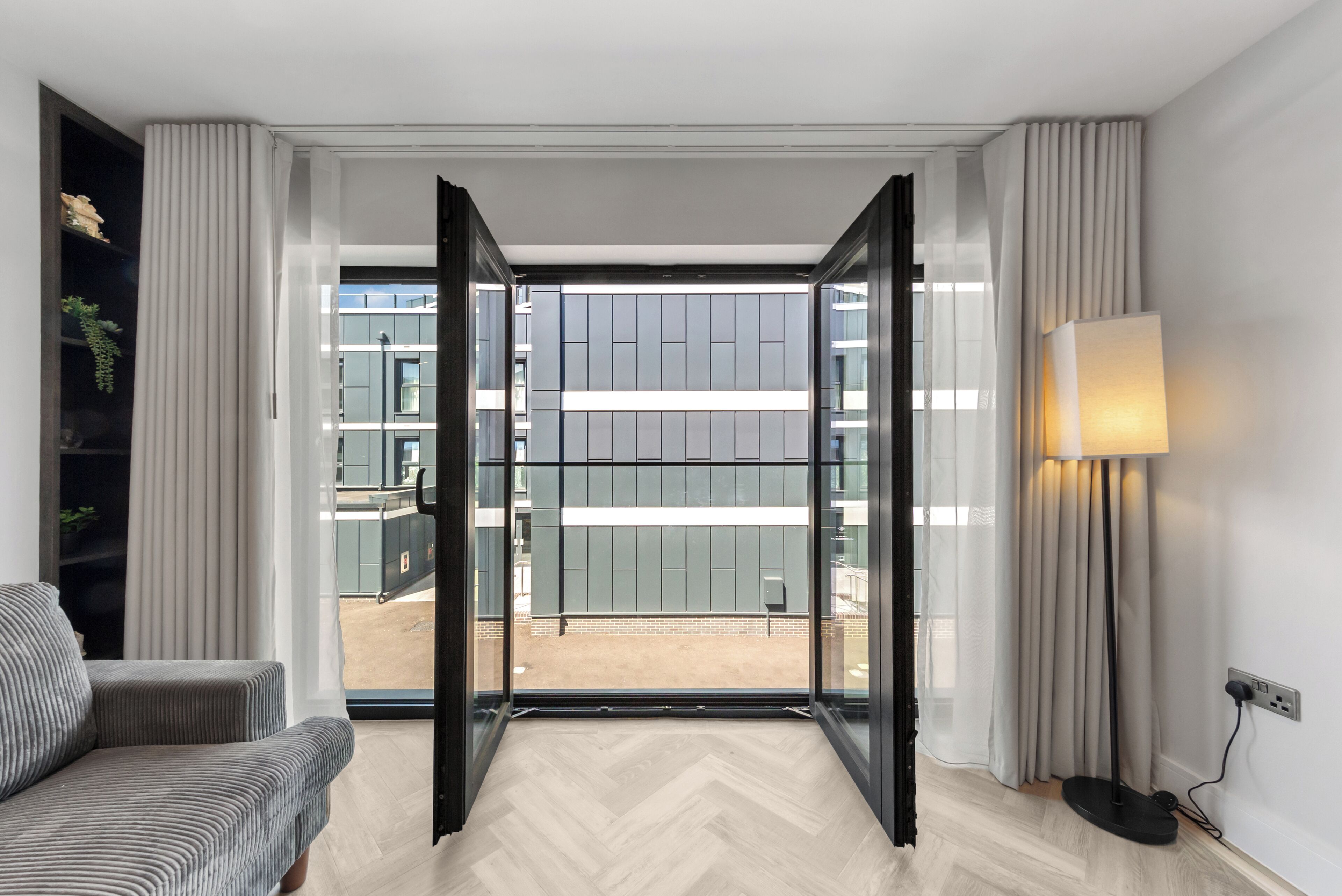A hotel room with a large sliding glass door leading to an outdoor terrace, a sofa, a lamp, and a plant.