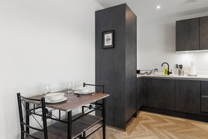 A modern kitchen with dark cabinetry, a dining table with chairs, and a framed inspirational quote on the wall. - Modern 1-Bed | 2 Mins to Cockfosters Tube (Barnet)
