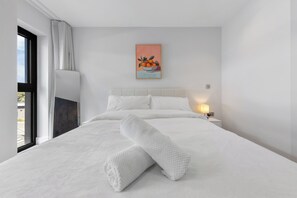 Habitació d'hotel moderna amb un llit gran, una tauleta de nit amb una làmpada, un quadre de fruita a la paret i una finestra amb cortines.