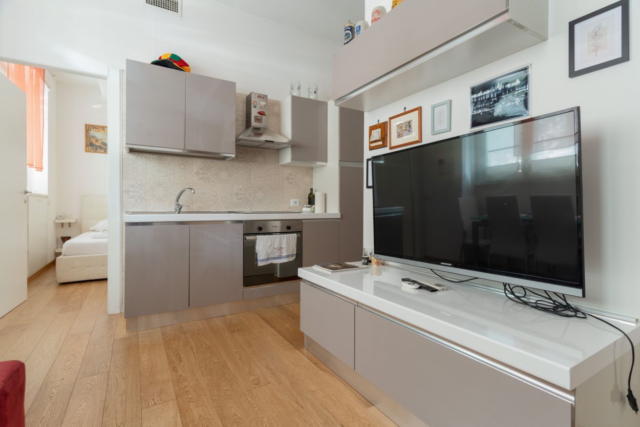 A modern kitchen with a large flat-screen TV, built-in oven, and a small island counter.