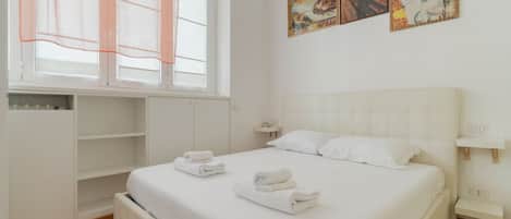 A bedroom with a bed, a window with blinds, a bedside table, and artwork on the wall.