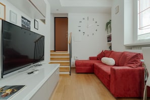 A modern living room with a flat-screen TV, a red sofa, a staircase, and a wall clock. - A comfortable 42 sqm apartment, ideal for 3 people, located on the raised ground floor of a building (steps required for access).The apartment is strategically located, 750 meters from the “Porta Romana” stop on the M3 (Yellow) metro line, which take (Milan)