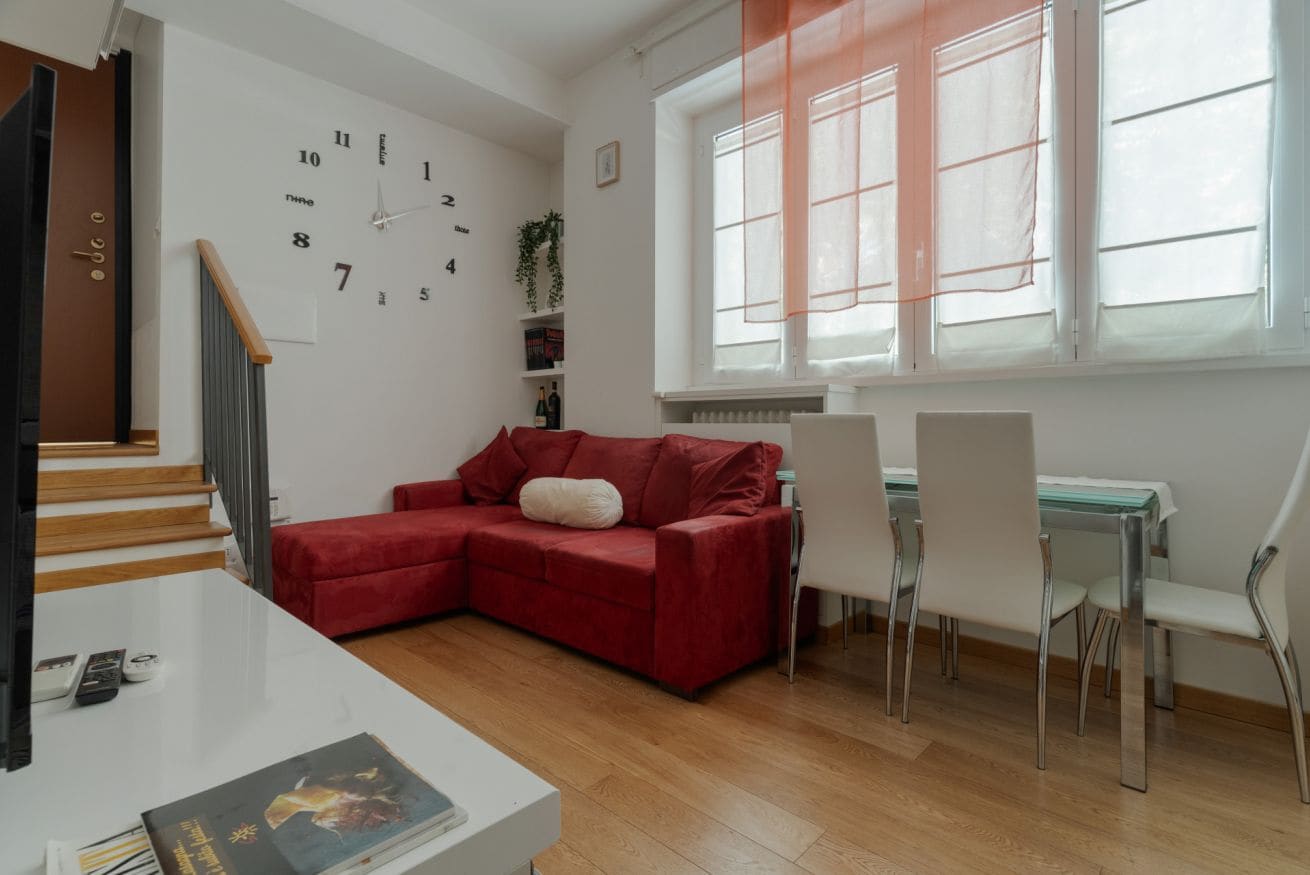 A modern living room with a red sofa, a white table, and a dining area with chairs.