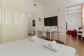 A hotel room with a bed, a desk, a chair, a TV, and a clock on the wall. - A comfortable 42 sqm apartment, ideal for 3 people, located on the raised ground floor of a building (steps required for access).The apartment is strategically located, 750 meters from the “Porta Romana” stop on the M3 (Yellow) metro line, which take (Milan)