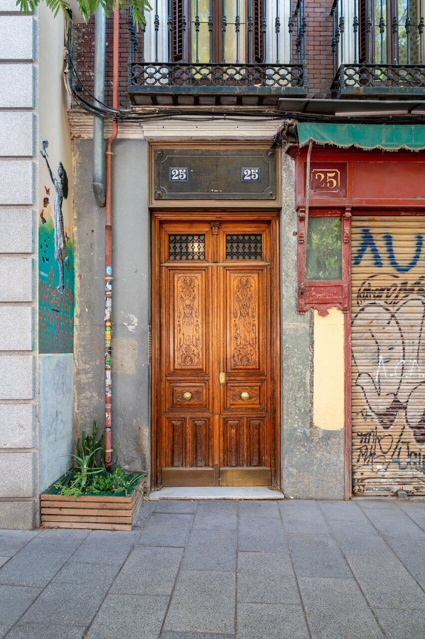 A wooden double door with a number '25' above it, a small step leading to the entrance, and a balcony with a metal railing.