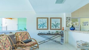 A living room with a sofa, a chair, a coffee table, and a bookshelf. There are two framed botanical prints on the wall. - Casa em Ubatuba com Piscina e Vista para o Mar (Ubatuba)