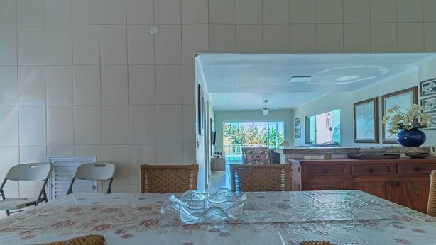 A dining area with a table set for four, surrounded by wicker chairs. A large vase with flowers is on the table. - Casa em Ubatuba com Piscina e Vista para o Mar (Ubatuba)