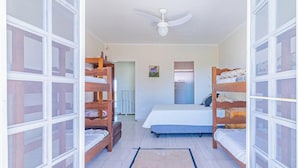 A room with bunk beds, a ceiling fan, a bed with a blue mattress, and a small painting on the wall. - Casa em Ubatuba com Piscina e Vista para o Mar (Ubatuba)