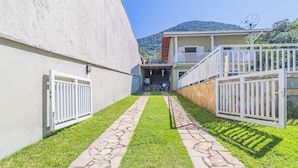 A pathway leading to a building with a stone-tiled entrance, a white fence, and a view of a mountain in the background. - Casa em Ubatuba com Piscina e Vista para o Mar (Ubatuba)