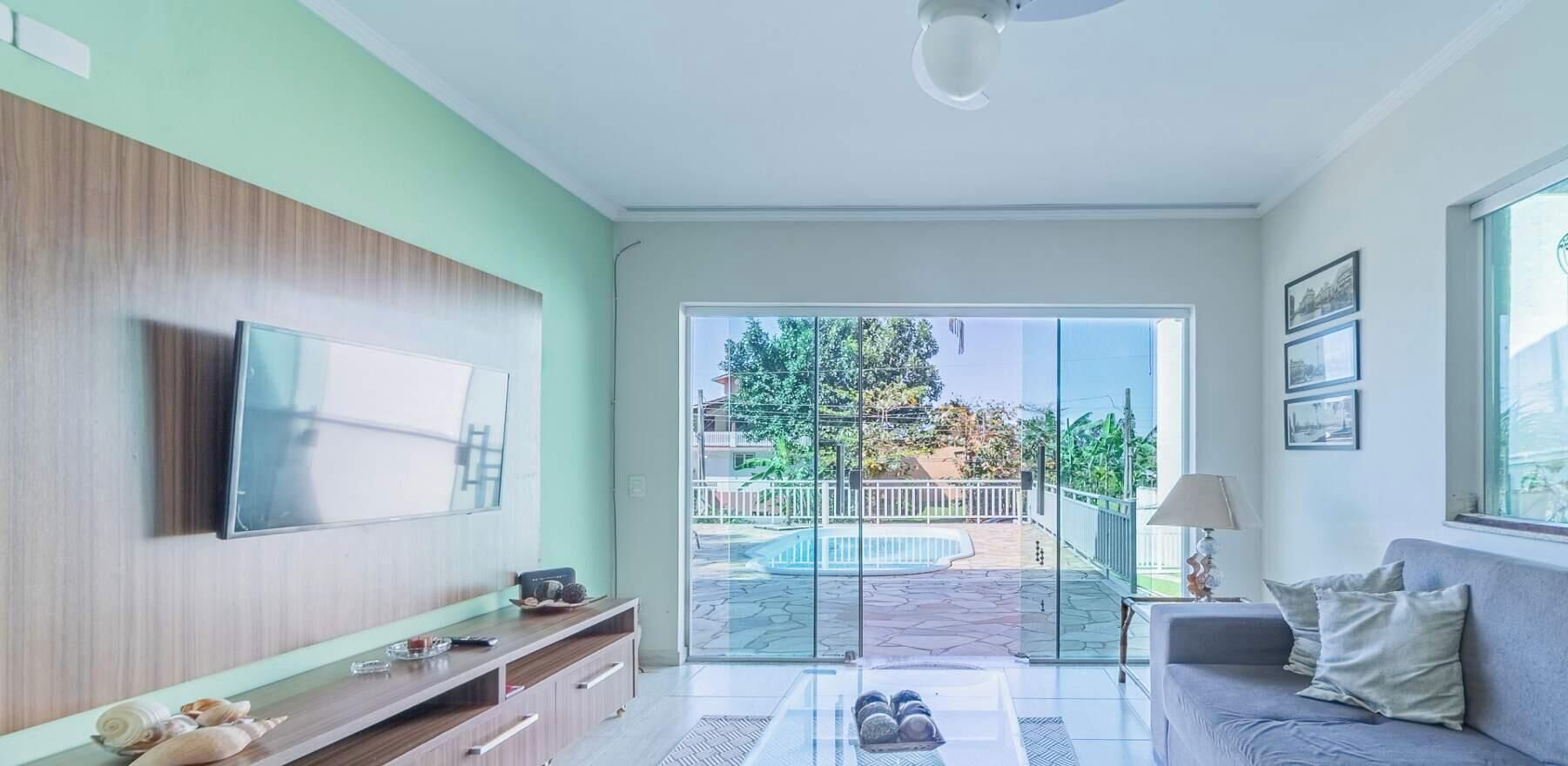 A modern living room with a flat-screen TV, a sofa, and a glass door leading to a pool area.