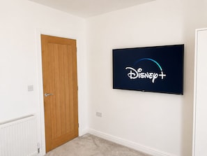 Una stanza con una porta in legno, un termosifone bianco e una televisione a muro che mostra il logo di Disney+.