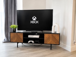 Un'unità moderna per l'intrattenimento con una TV a schermo piatto che mostra il logo Xbox, una console di gioco e una piccola pianta in vaso.