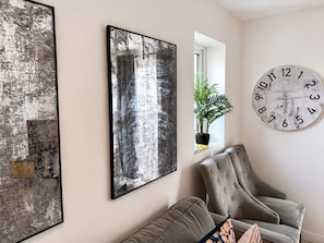 Une pièce comprenant un grand tableau abstrait, une horloge et un fauteuil.
