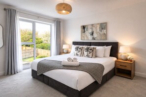 A bedroom with a large bed, two bedside lamps, a bedside table, a window with curtains, and a view of the outdoors. - 4 Bed House in Kent | Free Parking | Sleeps 8 | Long Stays (Sittingbourne)
