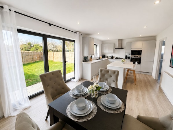 A modern kitchen with white cabinets and a dining area with a table set for four. - 4 Bed House in Kent | Free Parking | Sleeps 8 | Long Stays (Sittingbourne)