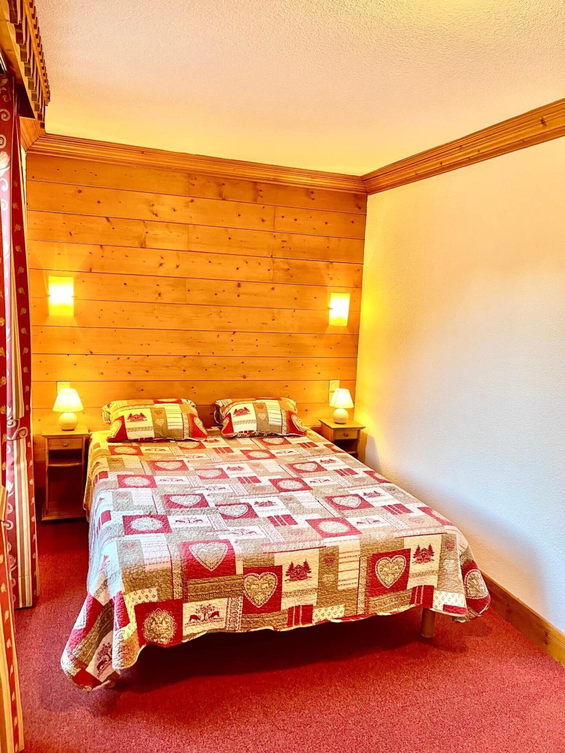 A bedroom with a wooden headboard, a quilted bedspread, two bedside lamps, and a red carpet.