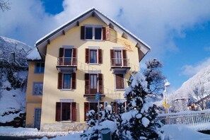 A multi-story building with balconies, a stone base, and snow-covered surroundings. - Chalet Le Joly Brides les Bains – 11 Bedrooms, Near Cable Car, Sleeps 23 (Brides-les-Bains)