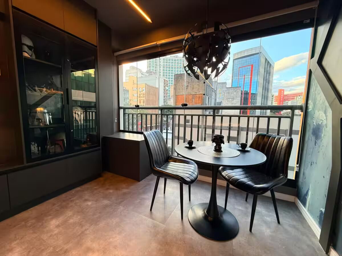 A modern room with a round table and chairs, a glass cabinet, and a view of the cityscape through large windows.