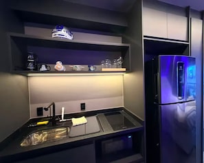 Une cuisine moderne équipée d’un réfrigérateur en acier inoxydable, d’un évier avec un robinet et d’une étagère contenant divers objets, notamment une tasse et une petite figurine.