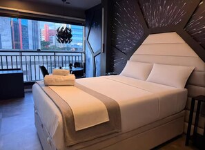 A modern bedroom with a large bed, a view of the city through a balcony, and a unique wall design. - Themed Studio | Liberdade Metro Station (São Paulo)
