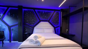 A modern hotel room with a large bed, a headboard with a geometric pattern, and a wall with a starry design. - Themed Studio | Liberdade Metro Station (São Paulo)