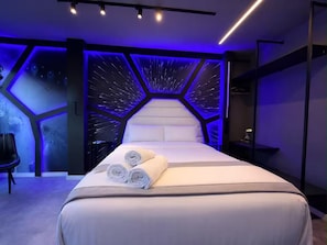 A modern hotel room with a large bed, a headboard with a geometric pattern, and a wall with a starry design. - Themed Studio | Liberdade Metro Station (São Paulo)
