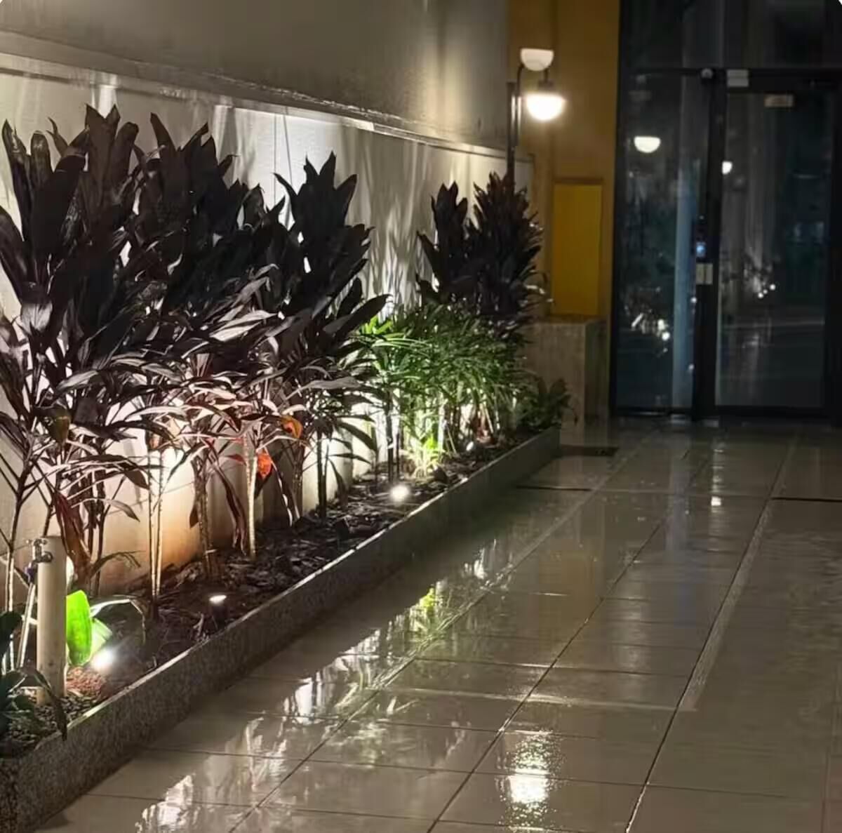 Ein Korridor mit einem spiegelnden Fliesenboden und einer Reihe von Blumentöpfen an der Wand.