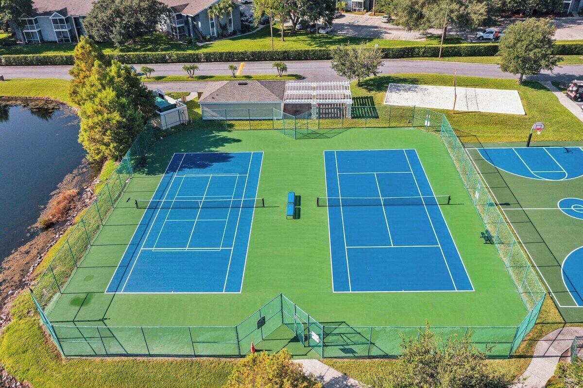 Ein Tennisplatzkomplex mit zwei Plätzen, einer überdachten Zuschauertribüne und einem Teich.