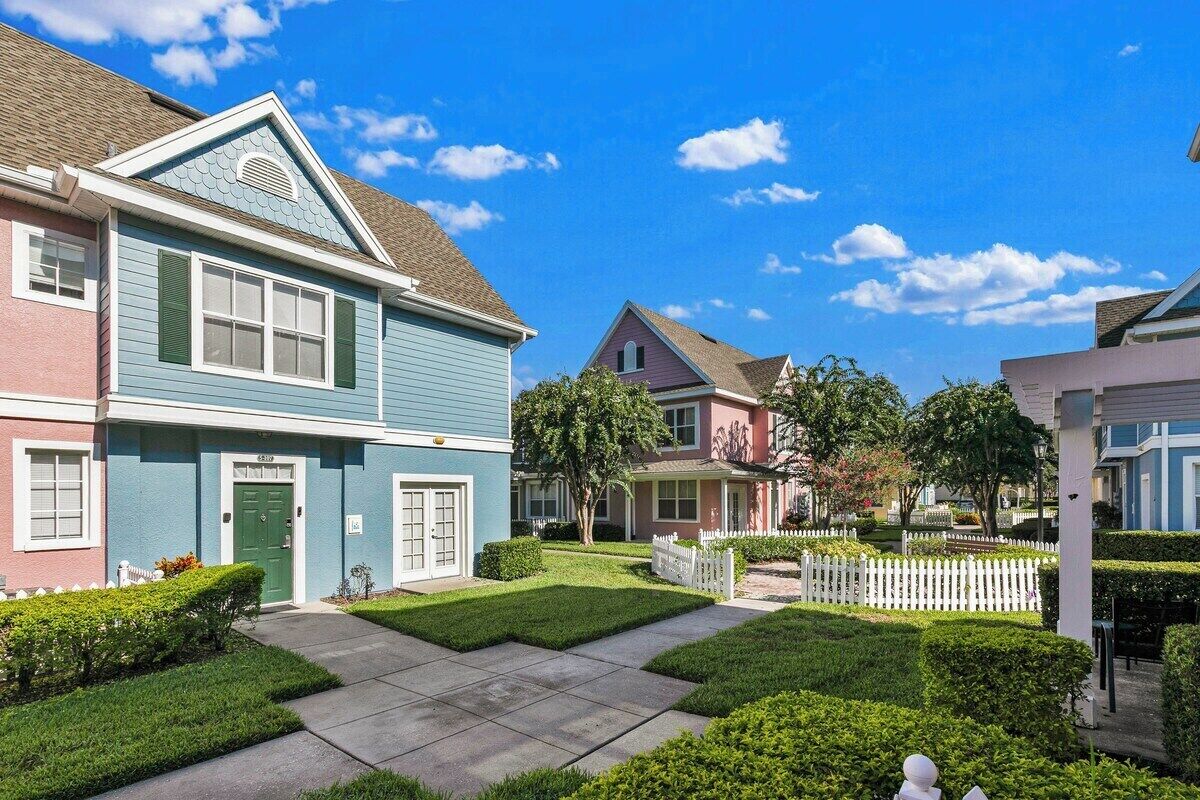 A residential street with houses, a white picket fence, and well-maintained lawns.