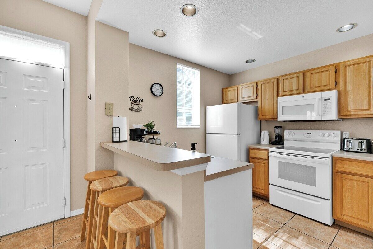 Una cocina moderna con una isla central, taburetes de madera, microondas, estufa y armarios de madera.
