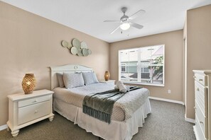 A bedroom with a bed, nightstand, dresser, ceiling fan, wall decor, and a window with blinds. - Venetian Bay Resort Townhouse w/ Pool & Gym Access (Kissimmee)