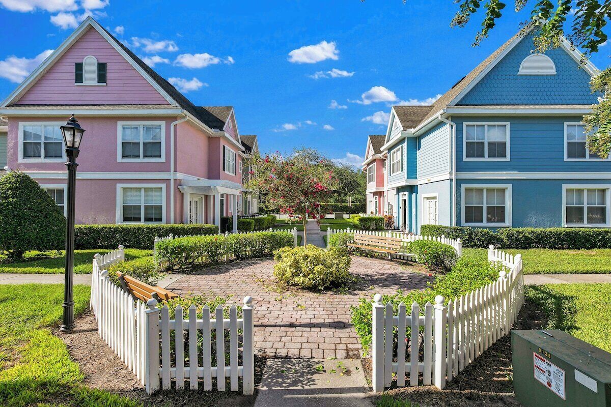 Un barrio residencial con dos casas, un camino pavimentado y una cerca blanca de piquetes.