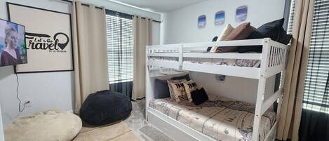 Een slaapkamer met stapelbed, televisie, gordijnen en een ingelijste foto aan de muur.