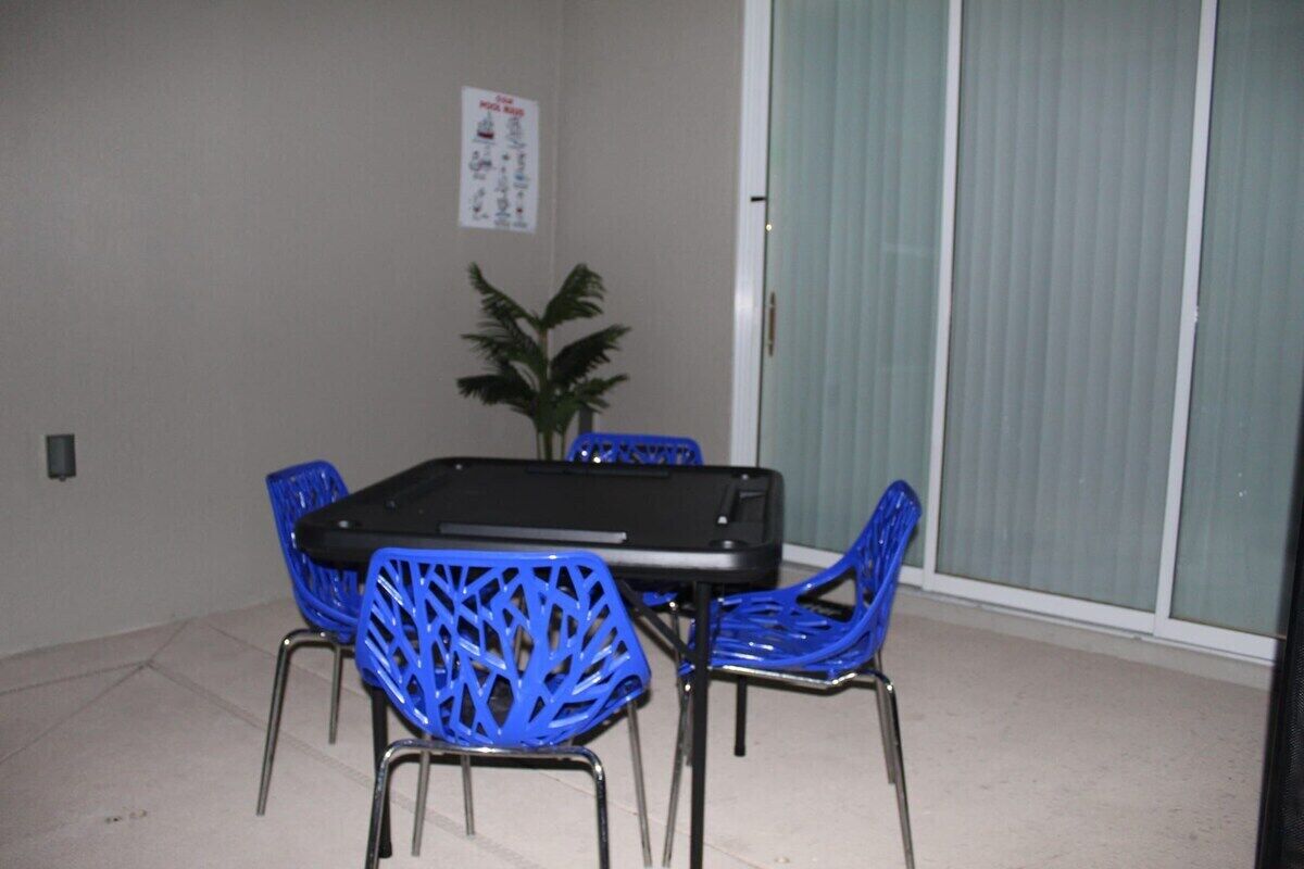 Un coin repas avec une table et quatre chaises bleues, une plante en pot et une affiche accrochée au mur.