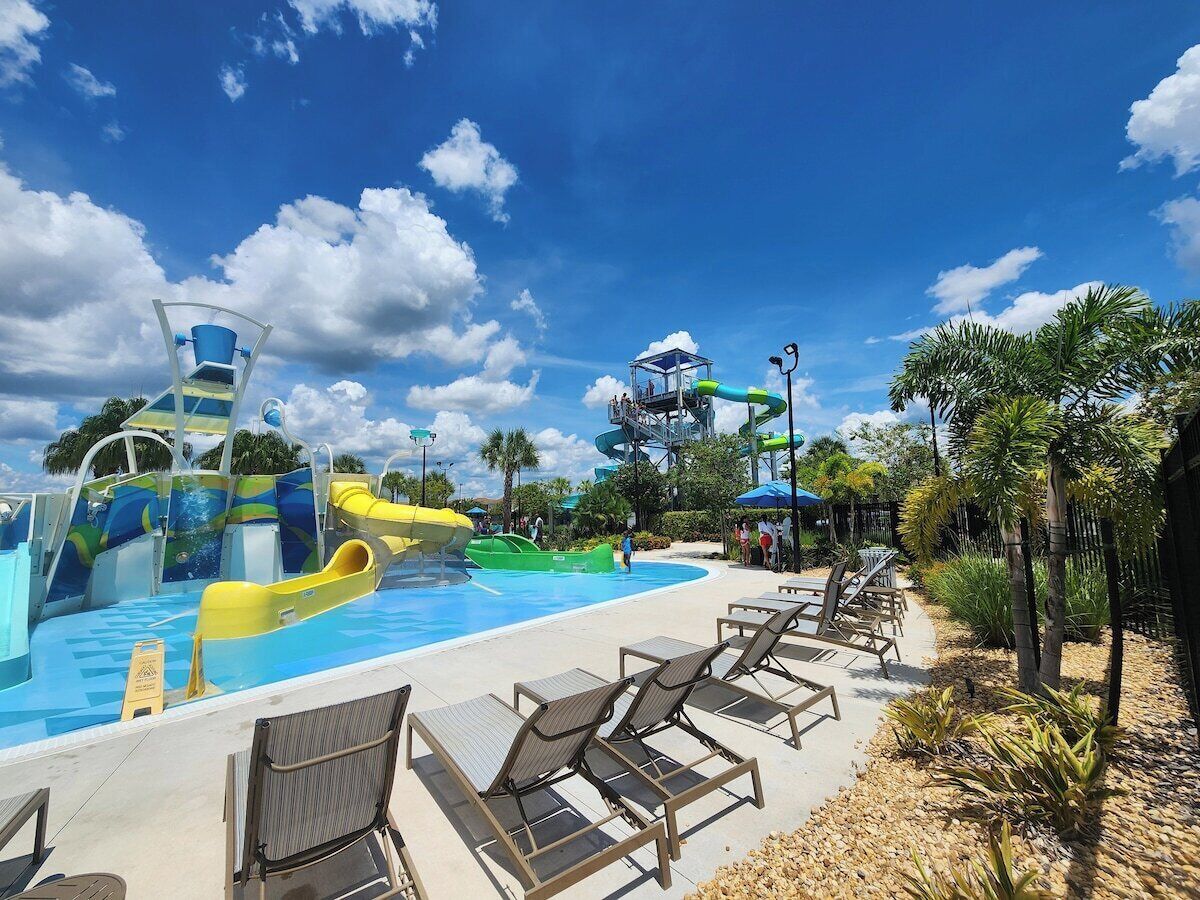 A water park with slides and a pool area, surrounded by palm trees and lounge chairs.