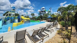 Parque acuático con toboganes y zona de piscina, rodeado de palmeras y sillones de descanso.