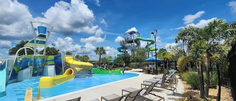 A water park with slides and a pool area, surrounded by palm trees and lounge chairs.