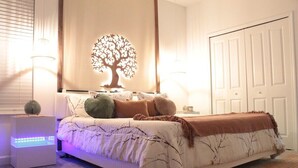 Un dormitorio con una cama, lámparas de noche, una decoración de árbol en la pared y un armario.