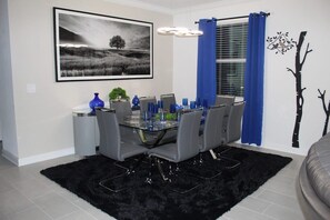 A dining area with a glass table, grey chairs, a black rug, a blue vase, and a framed black and white landscape painting. - Villa w/ Private Pool, Near Disney - Champions (Davenport)