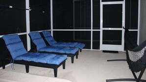 Un solárium con tres sillones azules acolchados y una butaca negra con asiento de mosquitera blanca.