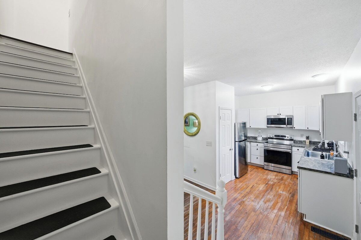 A staircase leading to a kitchen with white cabinets, stainless steel appliances, and a wooden floor.