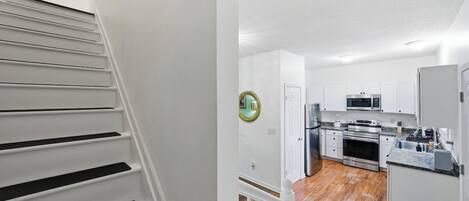 A staircase leading to a kitchen with white cabinets, stainless steel appliances, and a wooden floor.