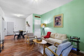 Ein Wohnzimmer mit grüner Wand, einer Couch, einem Couchtisch und einem Essbereich mit Stühlen und einem Tisch.