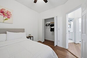 Ein Schlafzimmer mit Bett, Nachttisch, Deckenventilator, Gemälde und begehbarem Kleiderschrank.