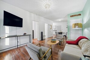 A modern living room with a flat-screen TV, a sofa, a coffee table, and a dining area with a table and chairs. - Affordable and Close to the City Townhome! (Atlanta)