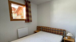 A single-bed room with a window, a headboard, a bedside table with a lamp, and a ceiling light. - Valfréjus – 6 people – Skiing & panoramic views (Modane)