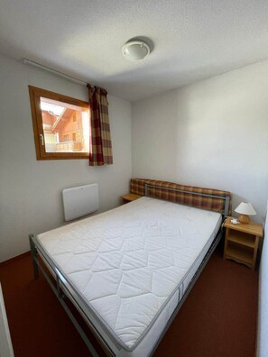 Einzimmer mit Fenster, Kopfteil, Nachttisch mit Lampe und Deckenleuchte.