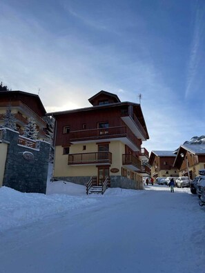 A multi-story building with balconies, a stone entrance, and snow-covered surroundings. - Valfréjus – 6 people – Skiing & panoramic views (Modane)